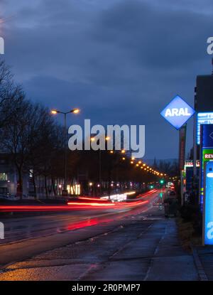 Kaiserslautern, Deutschland - 4. März 2021: Rote Lichtspuren von Autolichtern und Reflexionen auf der Straße neben einer Aral-Tankstelle in einer regnerischen Nacht i Stockfoto