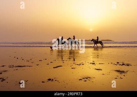 Essaouira, Marokko - 07. April 2023: Sonnenuntergang mit Silhouette aus Pferden und Reitern am Strand von Essaouira (Mogador), Marokko Stockfoto