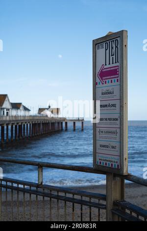 Outhwold, UK - Mai 2 2023 Ein Schild mit einem Pfeil, der auf den Pier zeigt, und eine Liste der Einrichtungen. Der Pier ist im Hintergrund zu sehen. Es ist Dämmerung A Stockfoto