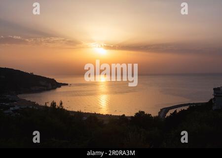 Orange Sonnenuntergang über dem Strand. Ein Sonnenuntergang über dem Meer mit Sonnenuntergang dahinter Stockfoto