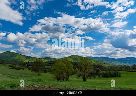 Eine wunderschöne natürliche Landschaft mit grünen Hügeln, die von Sonnenlicht und üppigen Wiesen umgeben sind, mit wunderschönen weißen, flauschigen Wolken am Himmel Stockfoto