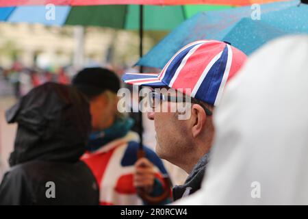 Mit einer Union-Jack-Mütze sieht ein Mann die Krönungsprozession von König Charles und Königin Camilla Stockfoto