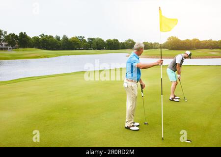 Er gibt sein Bestes. Zwei Freunde spielen zusammen Golf in ihrer Freizeit. Stockfoto