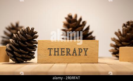 Die Inscription Therapy ist auf einer Holzfläche beschriftet. Pinienkegel-Konzept. Stockfoto