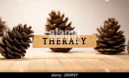 Die Inscription Therapy ist auf einer Holzfläche beschriftet. Pinienkegel-Konzept. Stockfoto