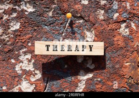 Die Inscription Therapy ist auf einer Holzfläche beschriftet. Felsoberfläche im Freien. Stockfoto