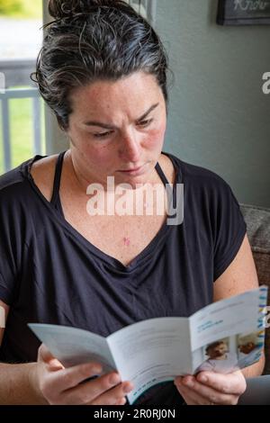 Nahaufnahme des vertikalen Bildes einer jungen 30s-Patientin, die Hautkrebsliteratur zu Hause auf der Couch nach neuerer Hautkrebsdiagnose liest. Stockfoto