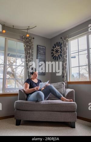 Vertikales Bild die junge 30s-Frau liest Literatur zu Hautkrebs aus der Dermatologie-Abteilung zu Hause auf der Couch nach der jüngsten Hautkrebsdiagnose auf ihrer che Stockfoto