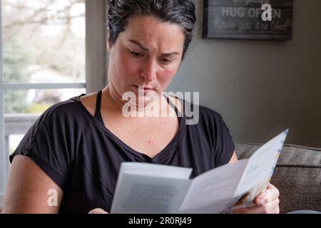 Nahaufnahme der horizontalen Darstellung einer jungen 30s-weiblichen Literatur zum Hautkrebs auf der Liege zu Hause bei neuerer Hautkrebsdiagnose. Stockfoto