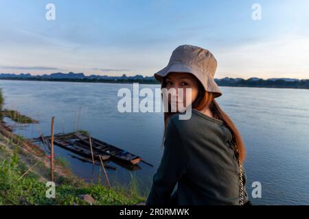 Eine attraktive Frau steht auf einem Hügel mit Blick auf einen Fluss und ihre Hände verschließen sich mit einer stilvollen Handtasche Stockfoto