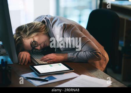 Ich brauche nur eine kurze Pause... eine junge Geschäftsfrau, die nachts an ihrem Schreibtisch in einem Büro schläft. Stockfoto