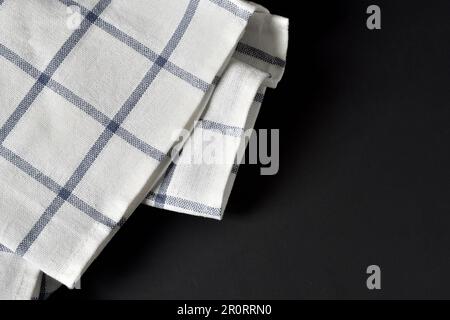 Schwarzer Tisch mit gestreiftem Küchenhandtuch. Textilserviette flach liegend. Gingham-Tischdecke auf schwarzem Hintergrund. Platz für Text kopieren.zum Kochen Stockfoto