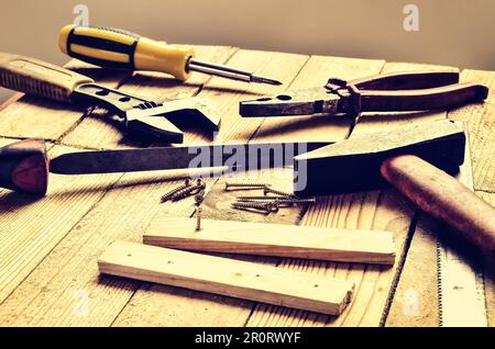 Renovierungswerkzeuge auf dem Tisch. Hammer, Flachfeile, Zange, Schraubendreher, Affenschlüssel, Schrauben, Dielen und Klinge auf natürlichem Holzhintergrund. Stockfoto