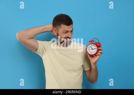 Emotionaler Mann mit Wecker auf hellblauem Hintergrund. Das Konzept der Verspätung Stockfoto