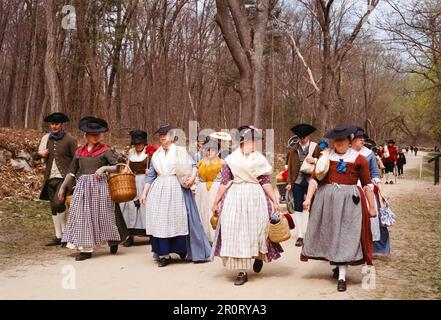 Lexington, Massachusetts, USA - April 2023 - Frauen und Kinder im Kolonialstil spazieren mit all ihren Gegenständen auf der Schlachtstraße in Minutenschnelle Stockfoto