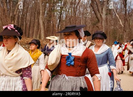 Lexington, Massachusetts, USA - April 2023 - Frauen und Kinder im Kolonialstil spazieren mit all ihren Gegenständen auf der Schlachtstraße in Minutenschnelle Stockfoto