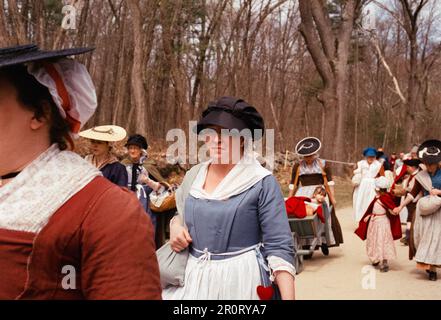 Lexington, Massachusetts, USA - April 2023 - Frauen und Kinder im Kolonialstil spazieren mit all ihren Gegenständen auf der Schlachtstraße in Minutenschnelle Stockfoto