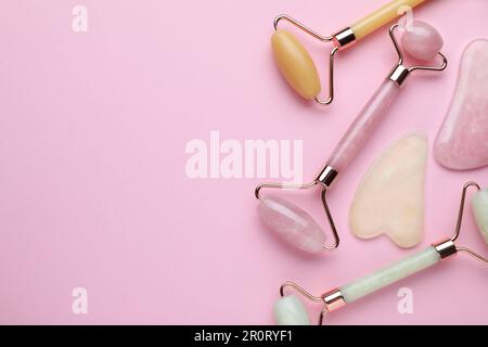 Verschiedene Gua-sha-Steine und Gesichtsrollen auf pinkfarbenem Hintergrund, flach liegend. Platz für Text Stockfoto