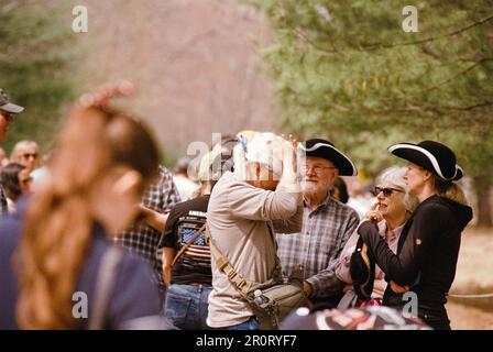 Lexington, Massachusetts, USA - April 2023 - Ein Mann zieht eine weiße Kolonialperücke an, während er mit seiner Familie neben der Battle Road in The Minuteman steht Stockfoto
