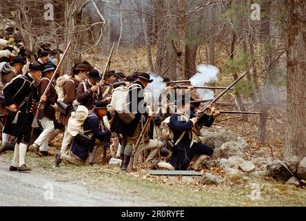 Lexington, Massachusetts, USA - April 2023: Im Minuteman National Histori stoßen koloniale und britische Truppen auf Musketen, die auf der Battle Road schießen Stockfoto