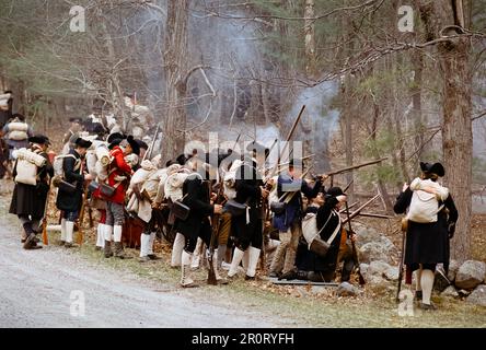 Lexington, Massachusetts, USA - April 2023: Im Minuteman National Histori stoßen koloniale und britische Truppen auf Musketen, die auf der Battle Road schießen Stockfoto