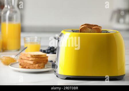 Gelber Toaster mit gerösteten Brotscheiben, Marmelade, Saft und Blaubeeren auf einem weißen Marmortisch Stockfoto