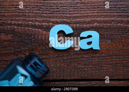 Papiersymbol Ca (Calcium) und medizinische Flasche mit Pillen auf Holztisch, Draufsicht Stockfoto