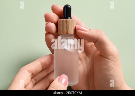 Eine Frau, die eine Flasche mit Serum vor dem Hintergrund von Oliven hält, Nahaufnahme Stockfoto