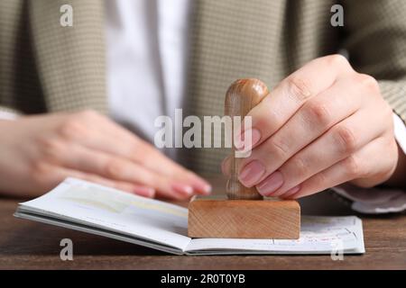 Ukraine, Lemberg - 6. September 2022: Frau stempelt Visumseite im Reisepass am Holztisch ab, Nahaufnahme Stockfoto