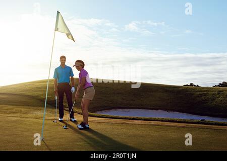Ich arbeite mit ihrer anderen Hälfte an ihrem Handicap. Ein Paar, das zusammen Golf auf einem Fairway spielt. Stockfoto