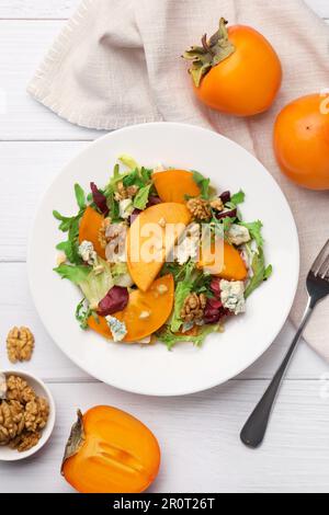 Köstlicher Persimonsalat und Gabel auf weißem Holztisch, flach liegend Stockfoto