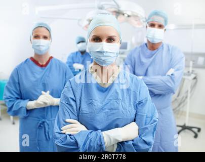 Vertrau uns mit deinem Leben. Gruppe von Chirurgen, die Krankenhauspeeling, Gesichtsmasken und Schutzhandschuhe in einer Notaufnahme tragen. Stockfoto