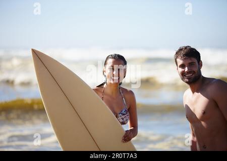 Ich liebe das Sommerwasser. Porträtaufnahme eines glücklichen jungen Paares, das mit einem Surfbrett im Meer posiert. Stockfoto