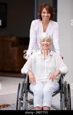 Jeder Grund, positiv zu sein. Eine Frau, die ihre ältere Mutter im Rollstuhl schubst. Stockfoto