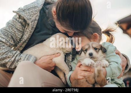 Nahaufnahme des Porträts einer Mutter mit ihrer Tochter, die zu Hause draußen mit niedlichen kleinen Hunden spielt. Lächelndes glückliches Kind. Fröhliche, lächelnde junge Frau Stockfoto