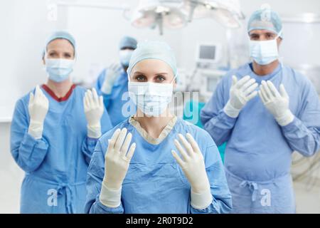 Hände, die gute Chirurgen sind. Porträt von vier Chirurgen, die ihre Hände mit weißen Schutzhandschuhen und Gesichtsmasken hochhalten. Stockfoto