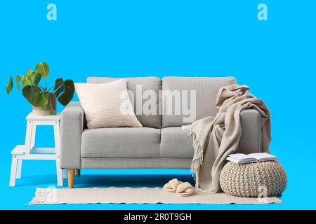 Gemütliches graues Sofa mit Karomuster, Kissen und Zimmerpflanzen auf blauem Hintergrund Stockfoto