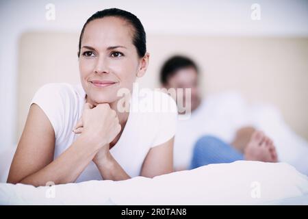 Ich denke an ihren bevorstehenden Tag. Eine junge Frau, die aufmerksam aussah, während sie mit ihrem Mann im Hintergrund auf einem Bett lag. Stockfoto