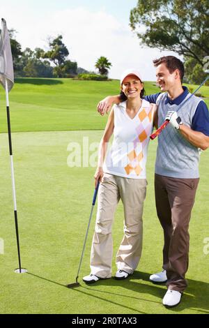 Ein Paar spielt Golf. Porträt eines Paares, das auf dem Golfplatz in der Nähe von flagstick steht und lächelt. Stockfoto