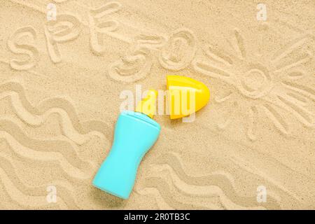 Kreative Komposition mit Sonnencreme und Zeichnungen auf Sand Stockfoto