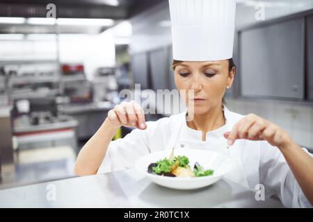 Perfekte Portionierung. Ein Koch, der den letzten Schliff auf einen Essteller in einer professionellen Küche legt. Stockfoto