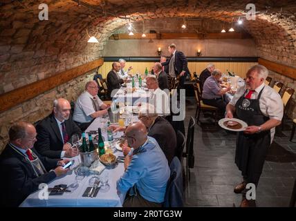 Trier, Deutschland. 08. Mai 2023. Die Männer des Spiessbratenclubs haben ihre Plätze im Gewölbekeller eingenommen, um gemeinsam den Roastbeef-Spießbraten zu konsumieren. Der Spiessbratenclub Trier ist der älteste Spiessbratenclub Deutschlands. (An dpa Text: Men on a Spit - Deutschlands ältester Spit Roast Club) Kredit: Harald Tittel/dpa/Alamy Live News Stockfoto