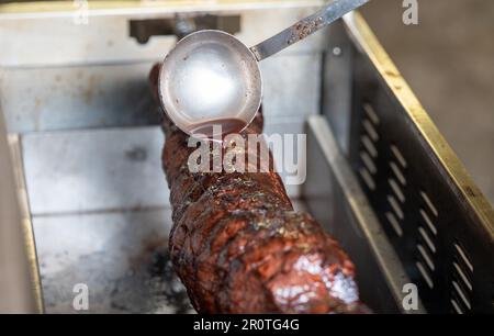 Trier, Deutschland. 08. Mai 2023. Ein Mitglied des Spiessbratenclubs Trier gießt Soße über den Braten. Der Spiessbratenclub Trier ist der älteste Spiessbratenclub Deutschlands. (An dpa Text: Men on a Spit - Deutschlands ältester Spit Roast Club) Kredit: Harald Tittel/dpa/Alamy Live News Stockfoto