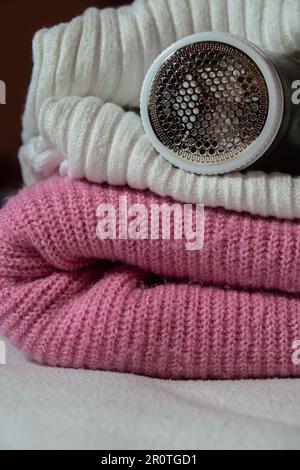 Anti-Pilling-Rasierer. Gerät zum Rasieren von Kleidung. Anti-Plush-Rasierer. Elektrischer tragbarer Pullover, Pille, Entfärbung, Fusselentferner aus pinkfarbenem Acryl- oder Wollpullover. Elektrorasierer nach der Reinigung und aufgefangenen Fusseln. Ein Pullover aus der Nahaufnahme. Alte gebrauchte Kleidung mit Pillen. Stockfoto