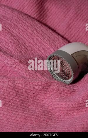 Anti-Pilling-Rasierer. Gerät zum Rasieren von Kleidung. Anti-Plush-Rasierer. Elektrischer tragbarer Pullover, Pille, Entfärbung, Fusselentferner aus pinkfarbenem Acryl- oder Wollpullover. Elektrorasierer nach der Reinigung und aufgefangenen Fusseln. Ein Pullover aus der Nahaufnahme. Alte gebrauchte Kleidung mit Pillen. Stockfoto