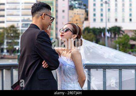 Vietnamesisches Hochzeitspaar, das vor der Skyline des Gebäudes von Ho Chi Minh City am Saigon River, Vietnam, posiert, um Fotos zu machen Stockfoto