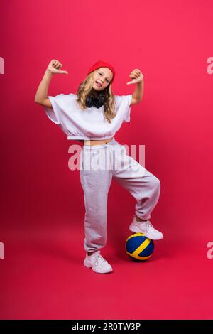 Ein Teenager hält den Volleyball in der Hand und lächelt auf rot gelbem Hintergrund. Studiofoto. Stockfoto