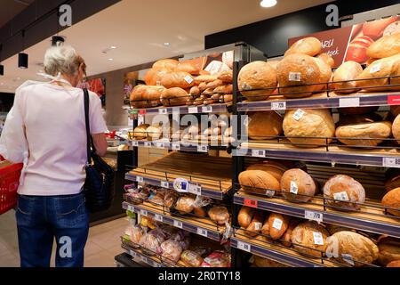 Budapest, Ungarn - 1. August 2022 - Brotlaibe und Baguettes auf der Brottheke in einem Supermarkt und ältere Frau mit Maske einkaufen Stockfoto