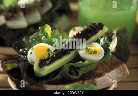 Sellerie gefüllt mit Tapenade, Wachteleiern und Salatblättern auf gegrilltem Brot Stockfoto