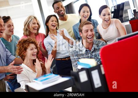 Das ist die Bonuszeit. Eine vielfältige Gruppe von Kollegen ist begeistert von etwas, das sie auf dem Computer sehen. Stockfoto